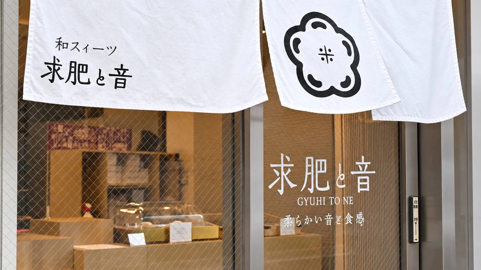 梅の紋を染め抜いた白い暖簾と、求肥と音のガラスの店名